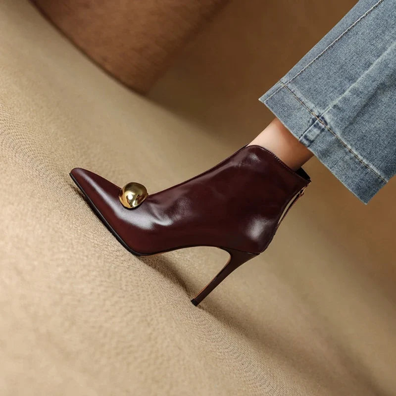 Model wearing burgundy pointed toe ankle boot with metal ornament