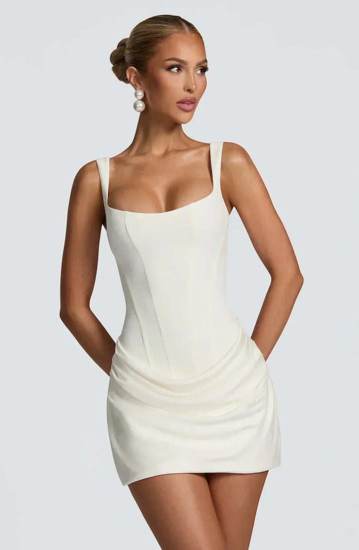 Robe courte femme drapée en blanc, avec corset ajusté et tissu léger pour une silhouette élégante et stylée.
